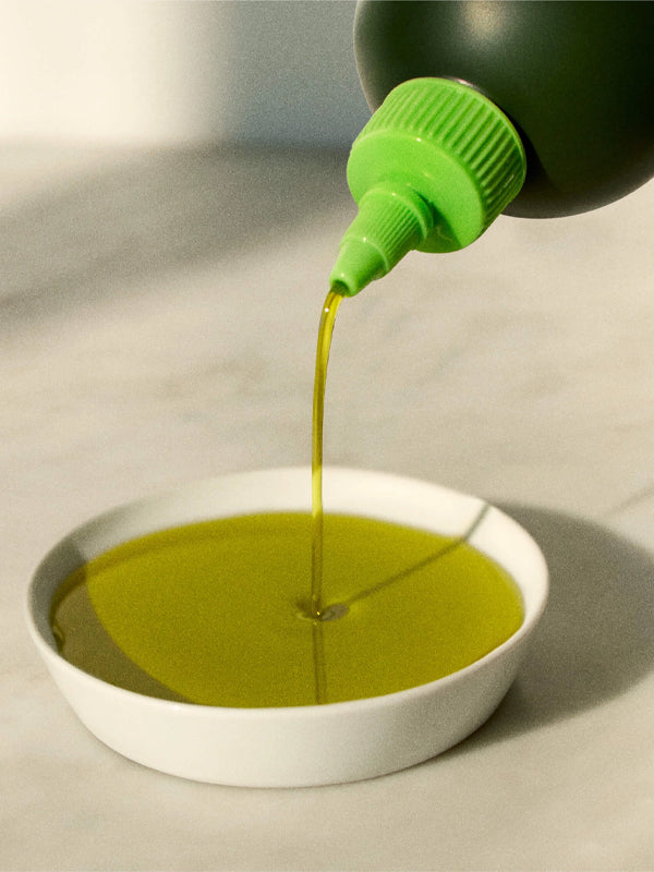 A sleek bottle of Graza Baby Drizzle olive oil, featuring a vibrant green label and a modern, ergonomic design. The olive oil is known for its rich, smooth flavor, perfect for drizzling over dishes or using as a finishing touch in cooking.