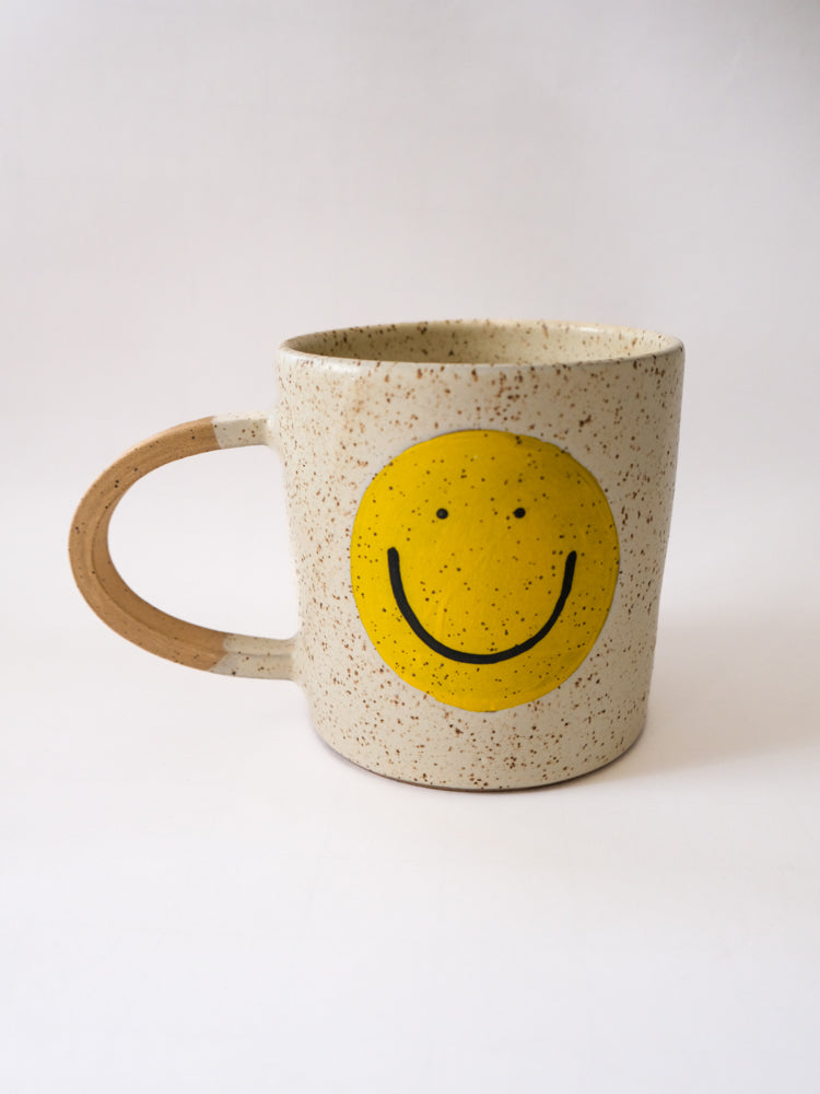 A white mug featuring a cheerful, smiling face design, perfect for adding a touch of positivity to your morning routine.